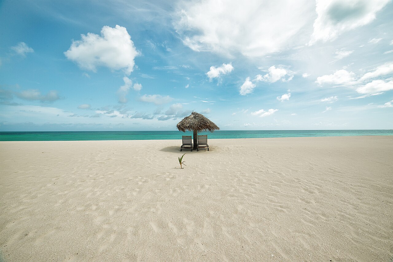 A quiet palapa and two chairs facing turquoise water on Barbuda’s pink-sand coast